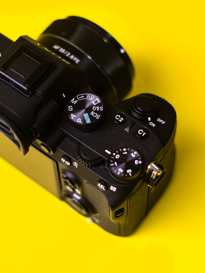Close-up of a black camera against a bright yellow background, showcasing its dials and controls.